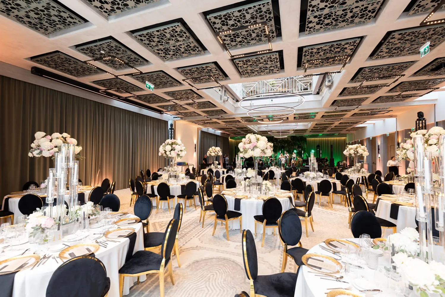 A pyramid stack of empty crystal champagne coupe glasses on a glass table with a dark background and soft lighting.