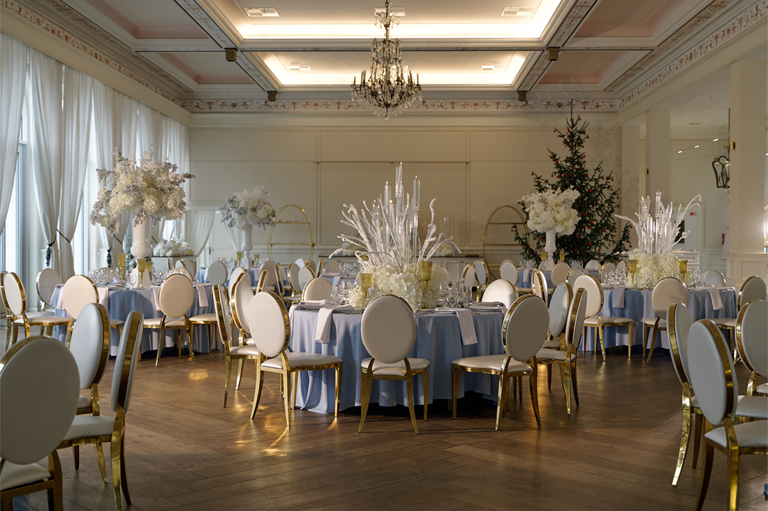 A pyramid stack of empty crystal champagne coupe glasses on a glass table with a dark background and soft lighting.