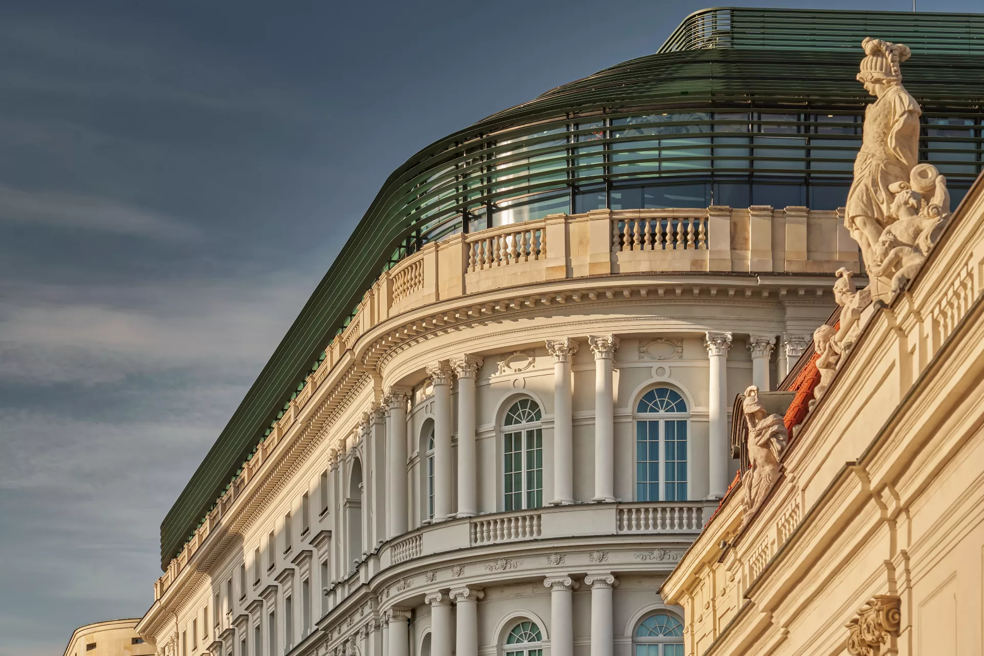 Elegant historical building with large arched windows and a striped tented outdoor seating area, surrounded by greenery and manicured lawns.