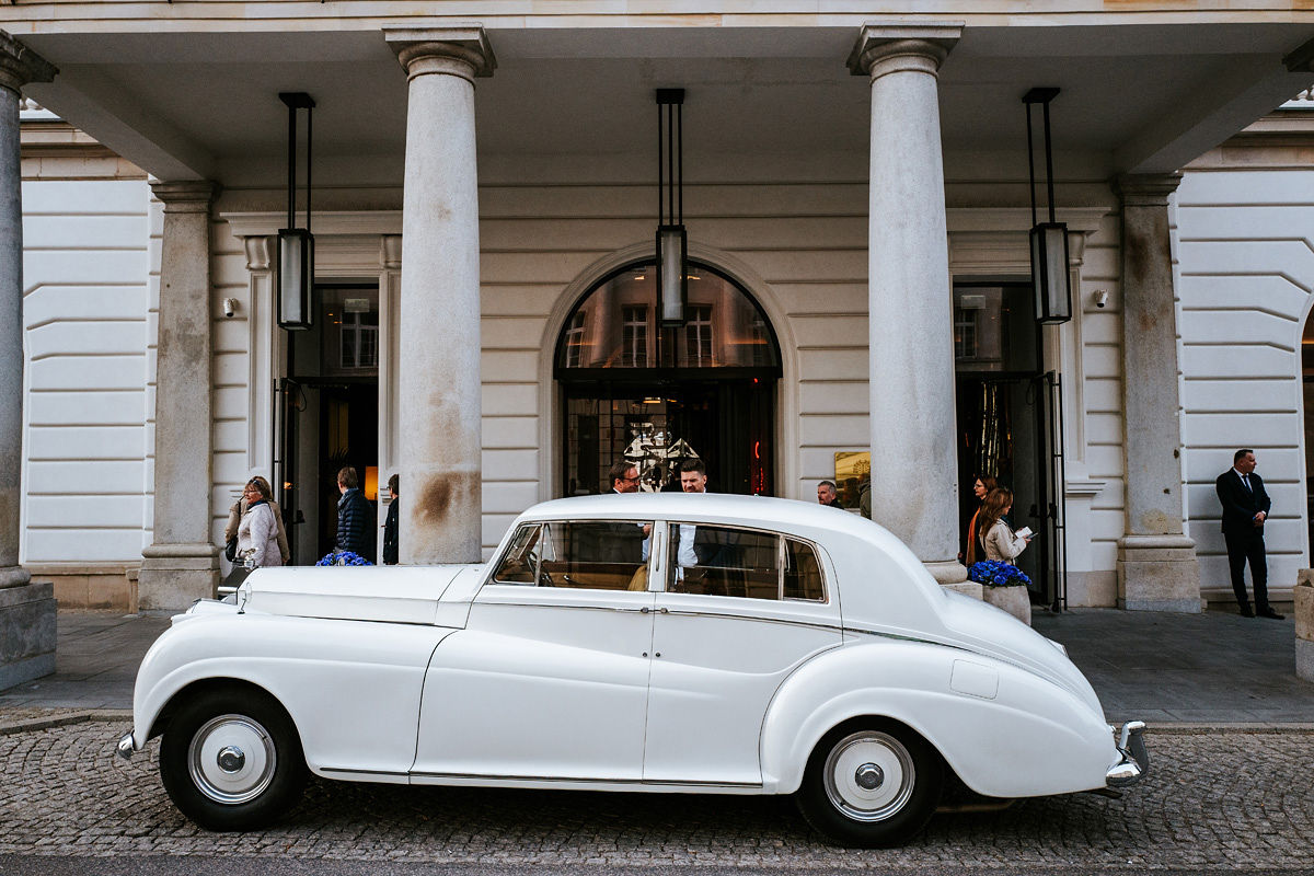Bride in a white wedding dress and veil sitting in the back seat of a car, looking to the side.