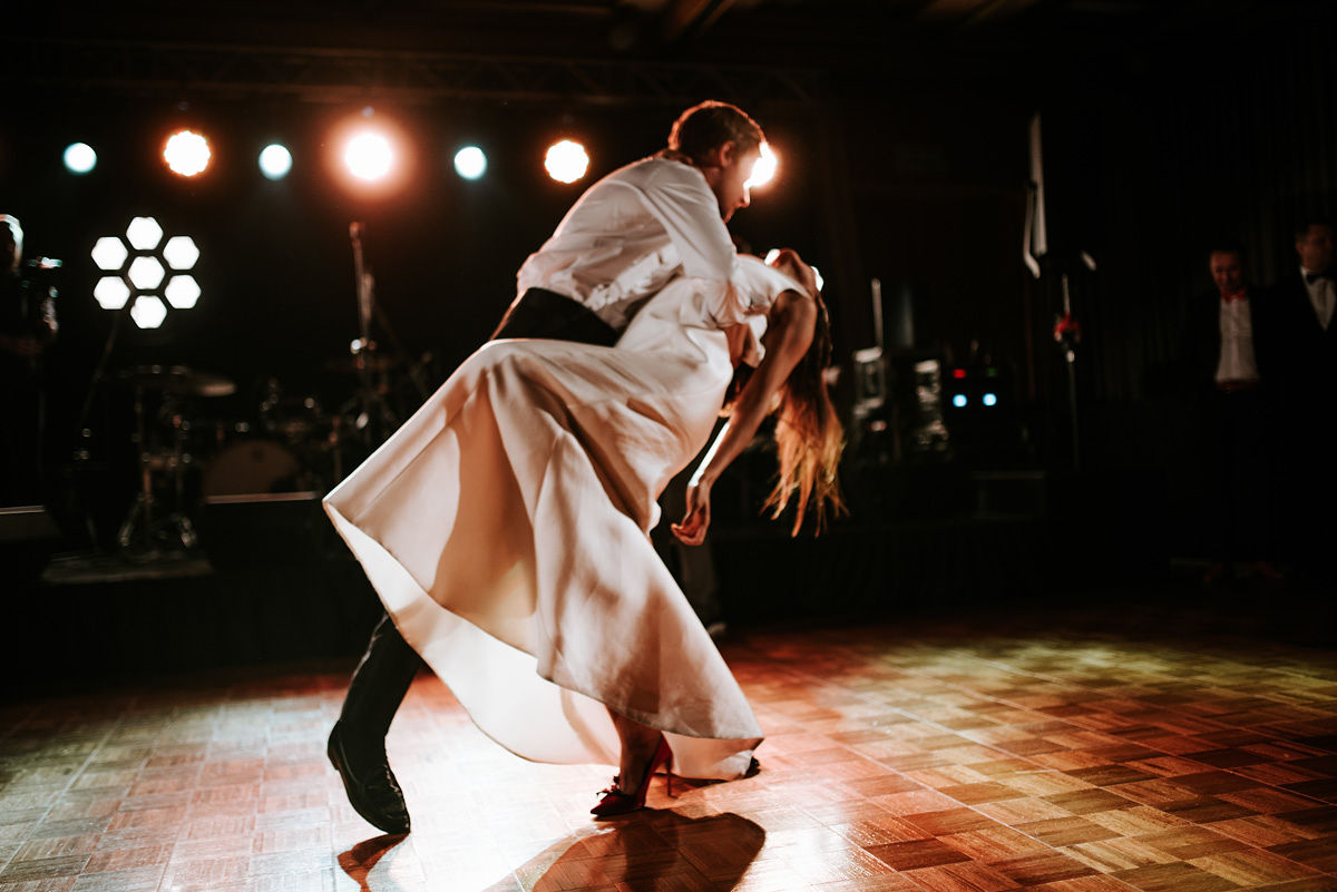 Young man in formal white shirt, black bow tie, and suspenders sitting in a blue armchair holding a phone.