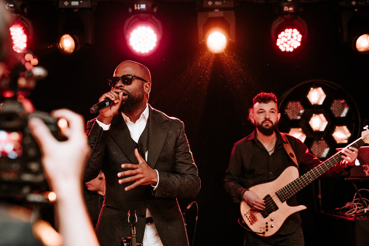 Young man in formal white shirt, black bow tie, and suspenders sitting in a blue armchair holding a phone.