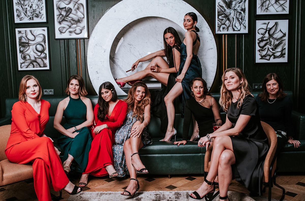 Young man in formal white shirt, black bow tie, and suspenders sitting in a blue armchair holding a phone.