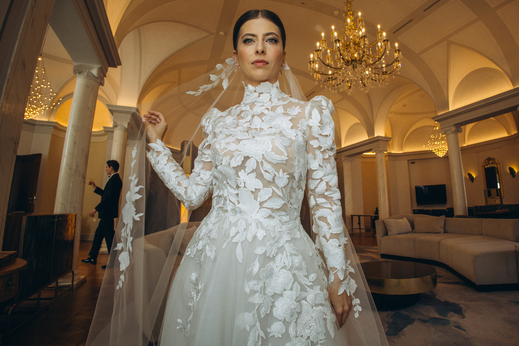 Bride and groom walking arm-in-arm down a white aisle decorated with tall vases of white flowers at an outdoor wedding ceremony.