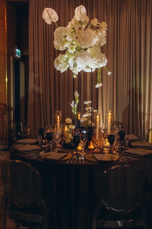 Woman in an elegant backless wedding dress standing by a window with sheer curtains looking outside at greenery.