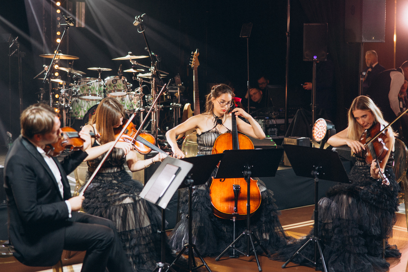 Woman in an elegant backless wedding dress standing by a window with sheer curtains looking outside at greenery.