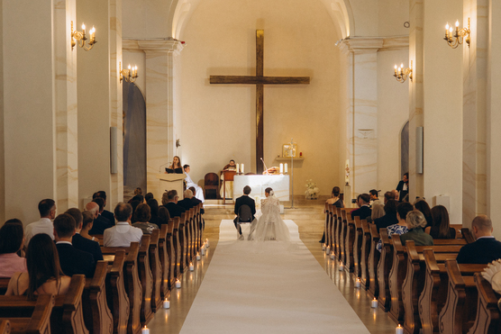 Bride and groom walking arm-in-arm down a white aisle decorated with tall vases of white flowers at an outdoor wedding ceremony.