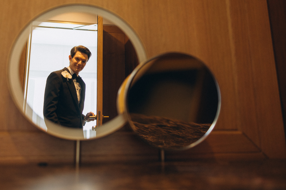 Outdoor wedding venue being set up with white chairs arranged on a paved area and a decorated white canopy at the end of a white aisle runner on grass.