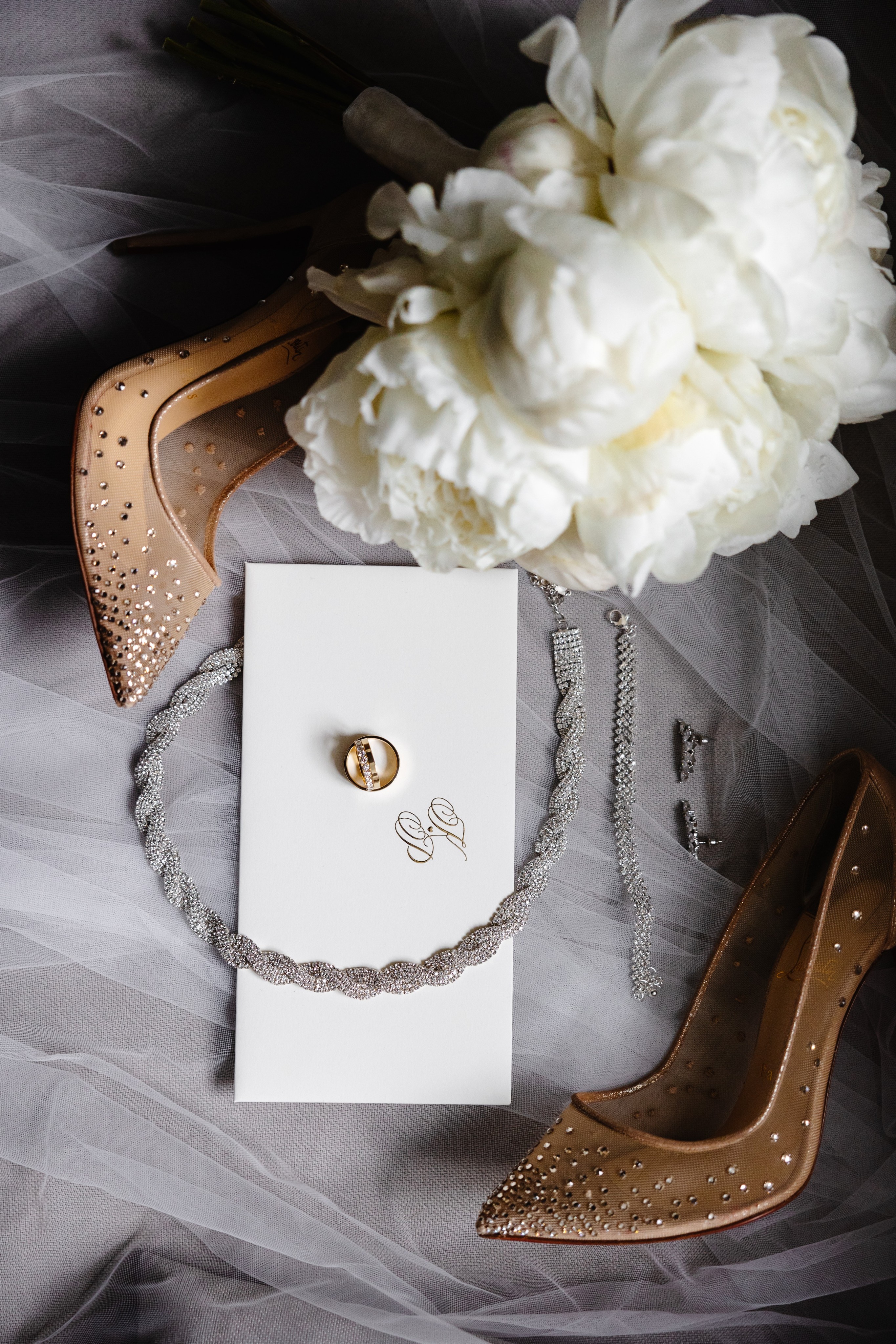 Bride in a white lace gown with a long veil and groom in a light beige suit holding champagne glasses at a decorated wedding venue.