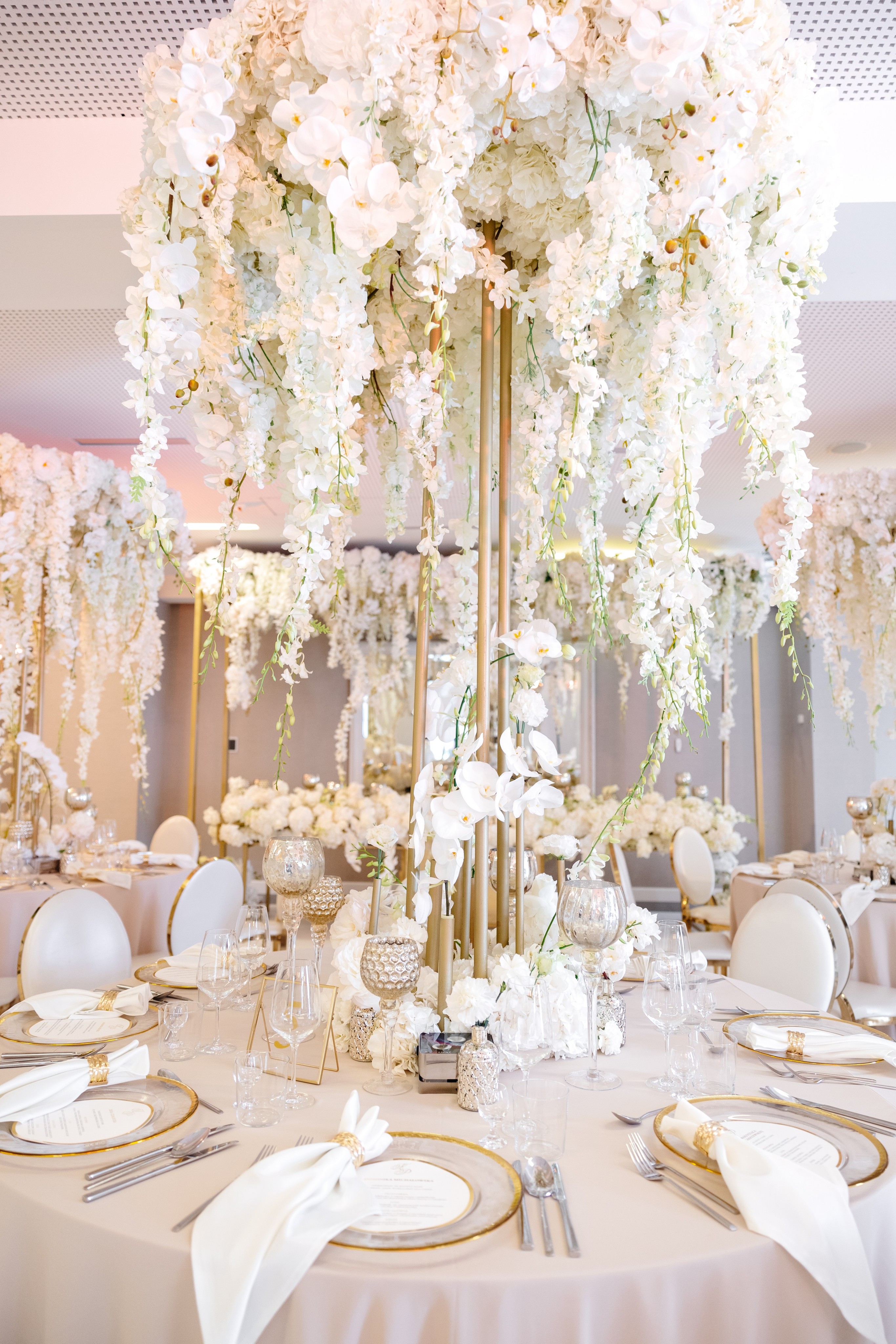 Couple dressed in white standing on a wooden pier overlooking a calm lake surrounded by trees at sunset.