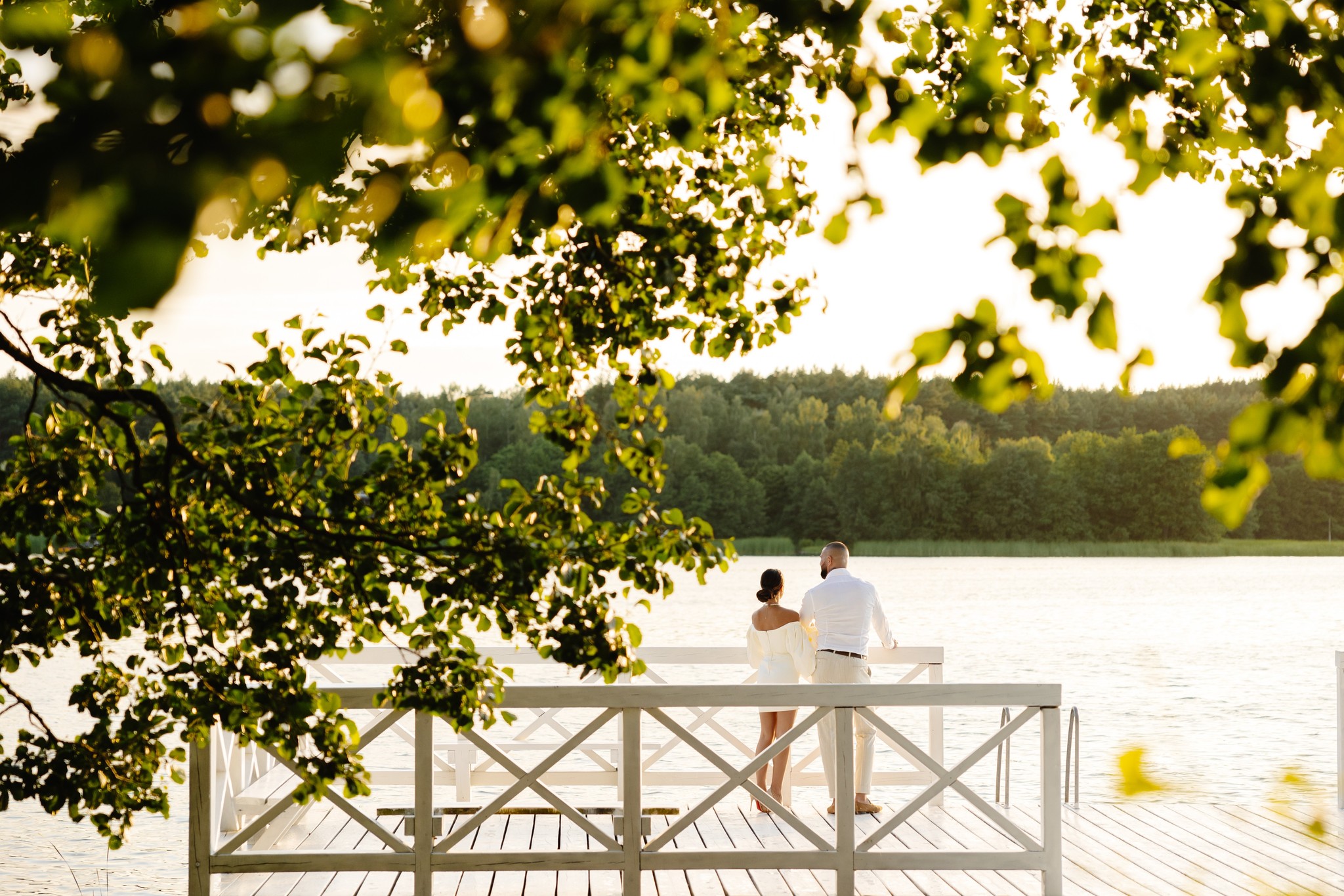 Bride and groom standing under a floral canopy exchanging vows at an outdoor wedding ceremony with seated guests watching.