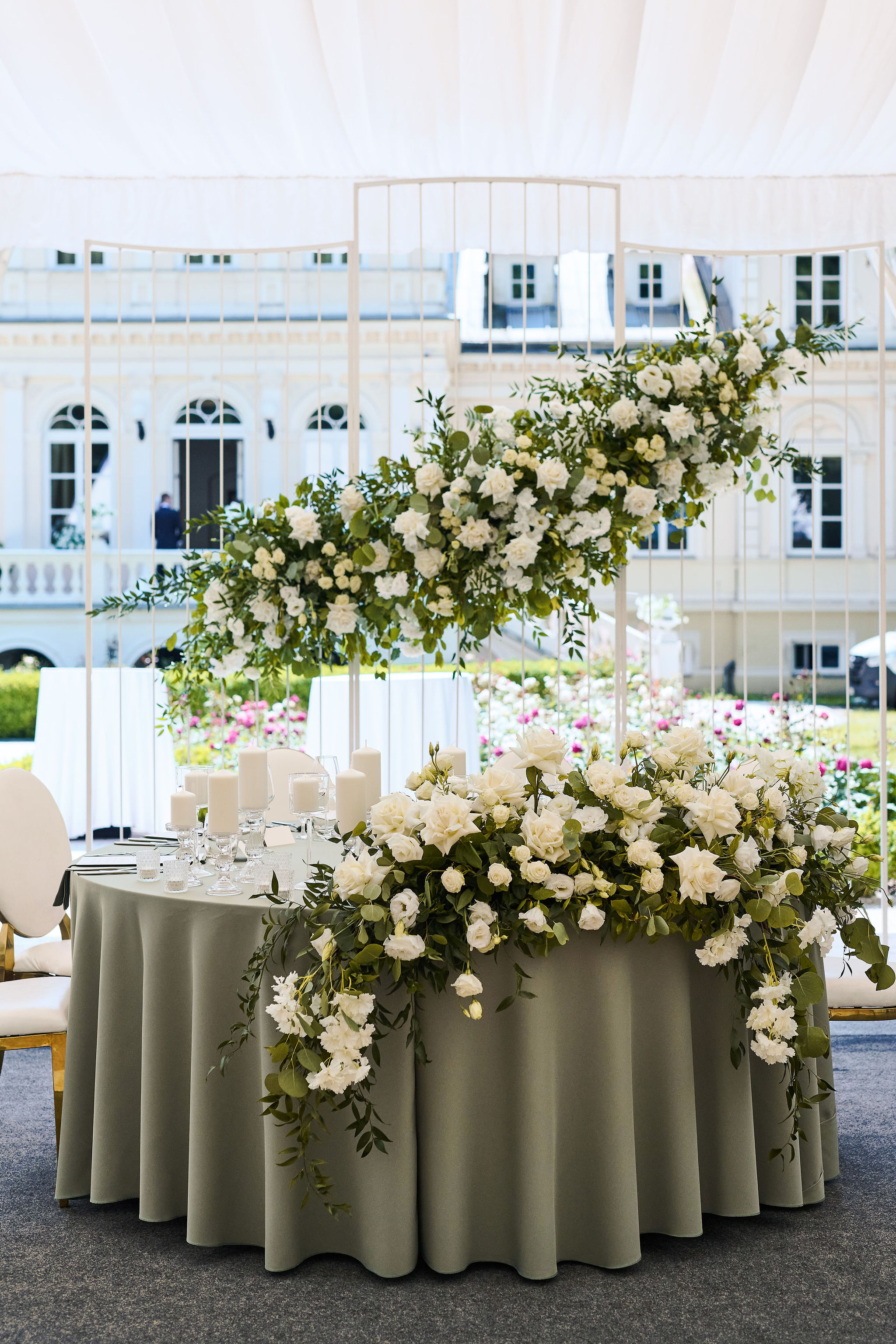 Bride in a white dress playing a white piano with crystal chandeliers above and two violinists performing in the background at an elegant wedding venue.