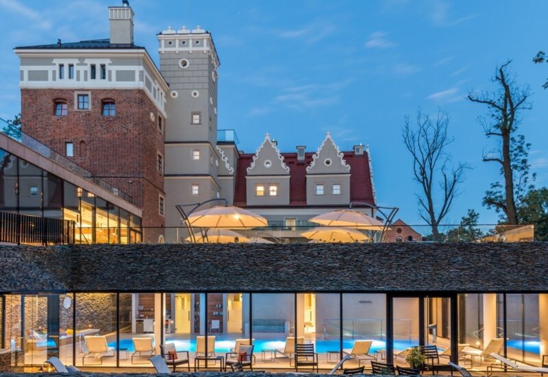A pyramid stack of empty crystal champagne coupe glasses on a glass table with a dark background and soft lighting.