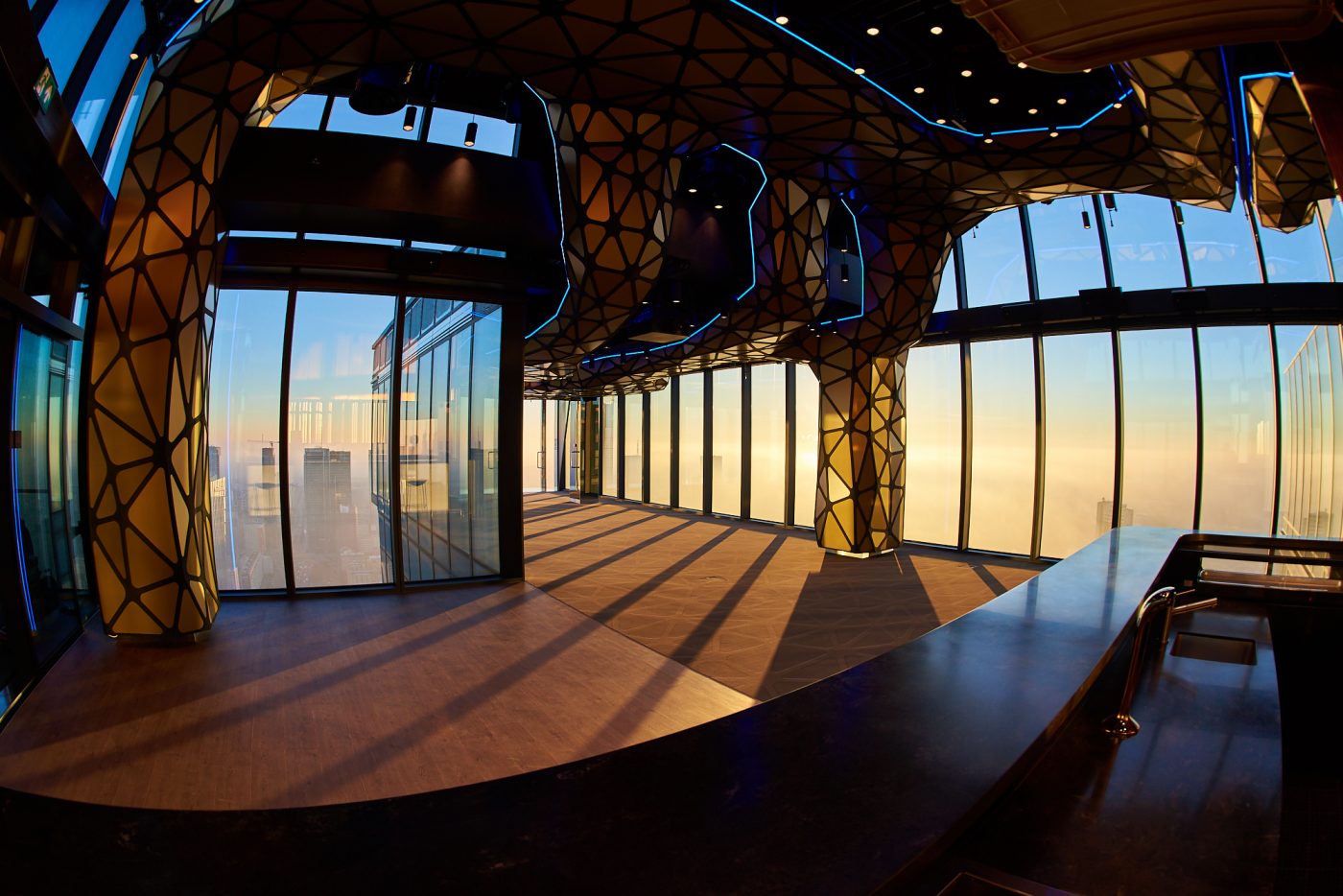 A pyramid stack of empty crystal champagne coupe glasses on a glass table with a dark background and soft lighting.
