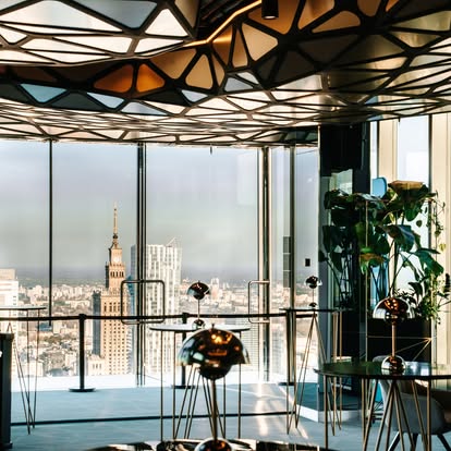 A pyramid stack of empty crystal champagne coupe glasses on a glass table with a dark background and soft lighting.