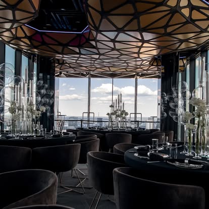 A pyramid stack of empty crystal champagne coupe glasses on a glass table with a dark background and soft lighting.