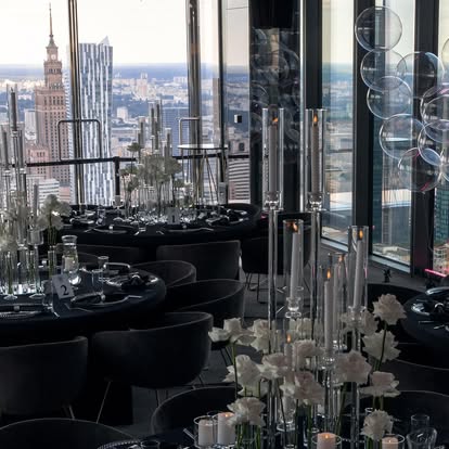 A pyramid stack of empty crystal champagne coupe glasses on a glass table with a dark background and soft lighting.