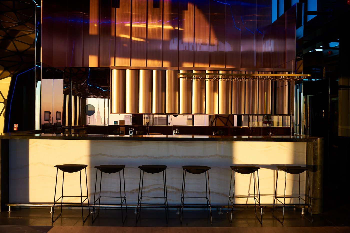 A pyramid stack of empty crystal champagne coupe glasses on a glass table with a dark background and soft lighting.