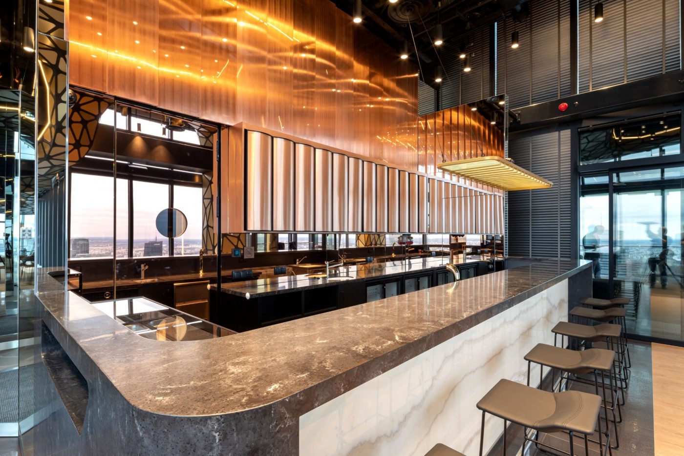 A pyramid stack of empty crystal champagne coupe glasses on a glass table with a dark background and soft lighting.