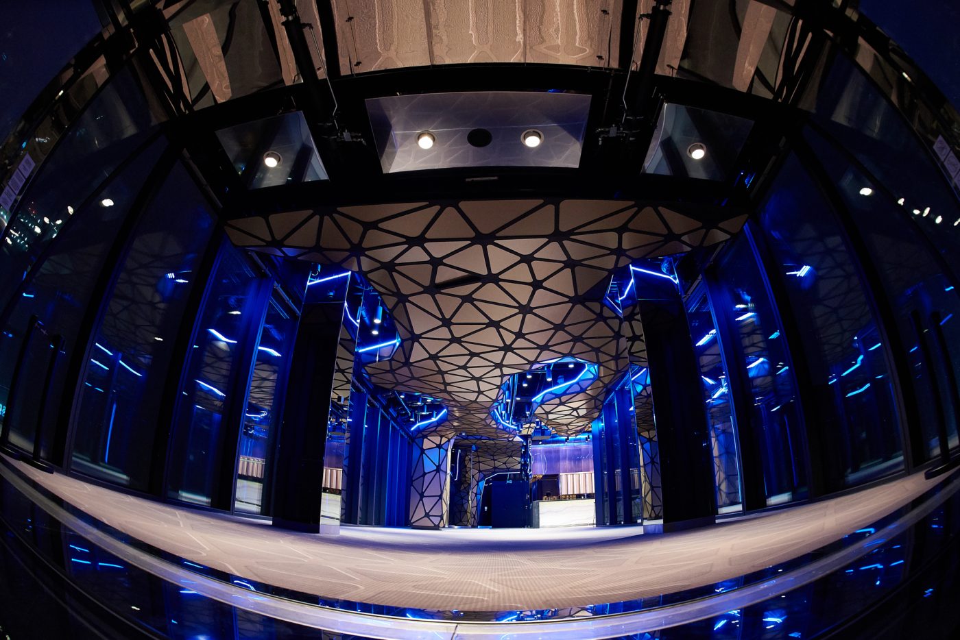 A pyramid stack of empty crystal champagne coupe glasses on a glass table with a dark background and soft lighting.
