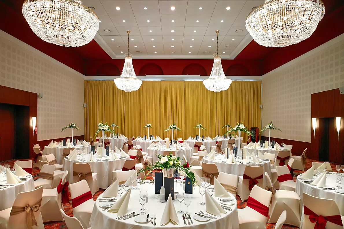 A pyramid stack of empty crystal champagne coupe glasses on a glass table with a dark background and soft lighting.