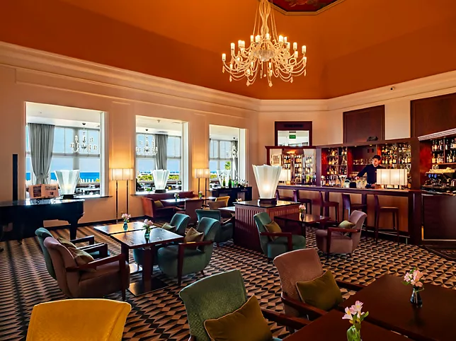 A pyramid stack of empty crystal champagne coupe glasses on a glass table with a dark background and soft lighting.
