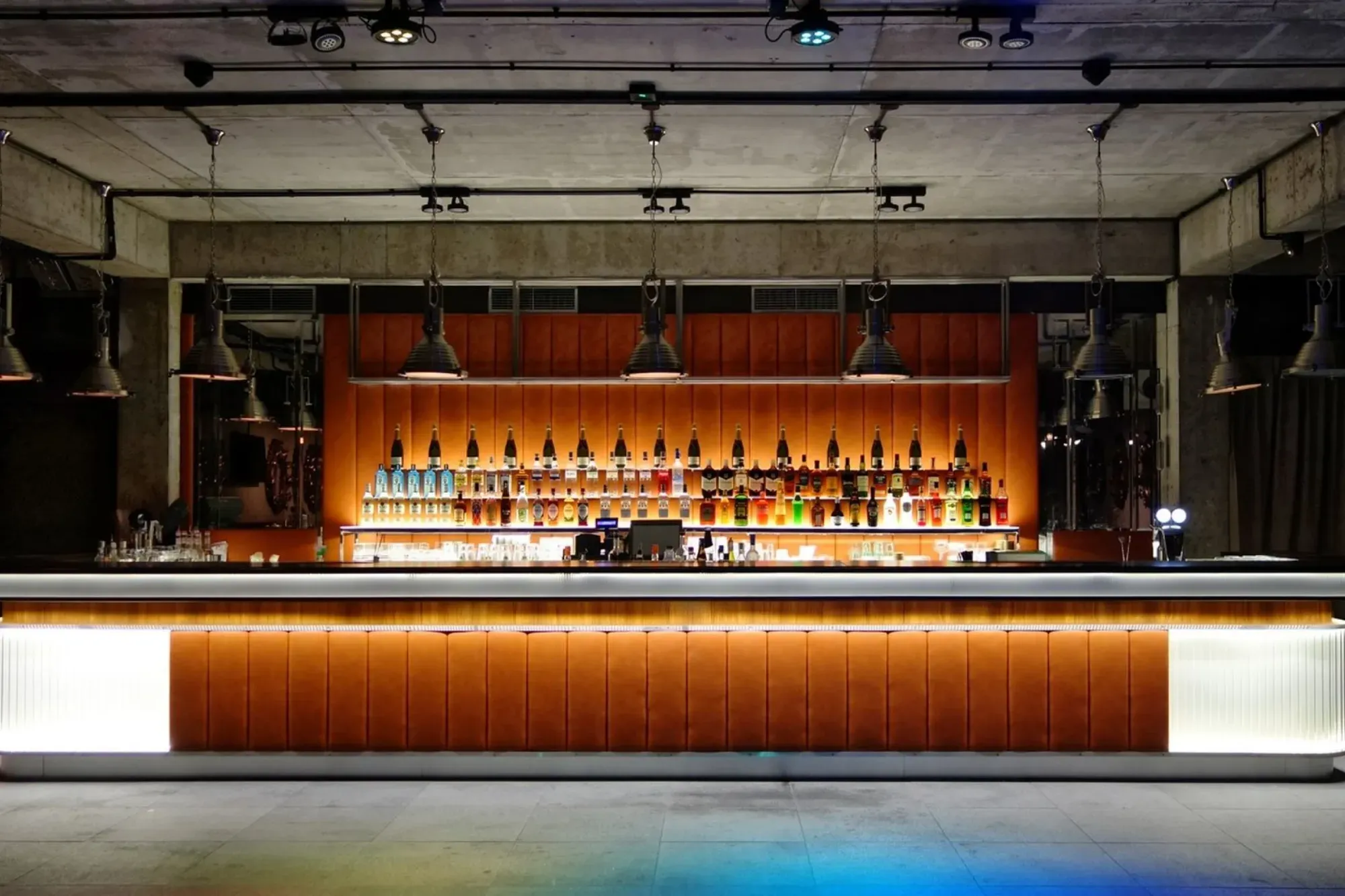A pyramid stack of empty crystal champagne coupe glasses on a glass table with a dark background and soft lighting.