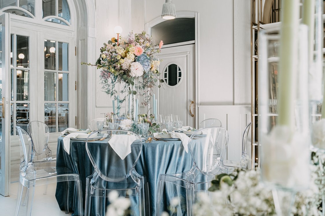A pyramid stack of empty crystal champagne coupe glasses on a glass table with a dark background and soft lighting.