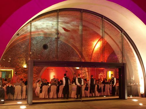 A pyramid stack of empty crystal champagne coupe glasses on a glass table with a dark background and soft lighting.