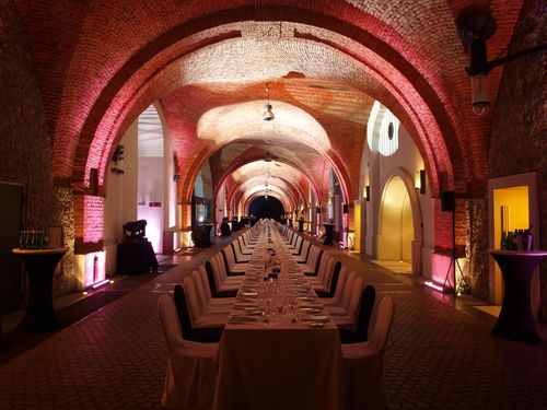 A pyramid stack of empty crystal champagne coupe glasses on a glass table with a dark background and soft lighting.
