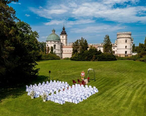 A pyramid stack of empty crystal champagne coupe glasses on a glass table with a dark background and soft lighting.