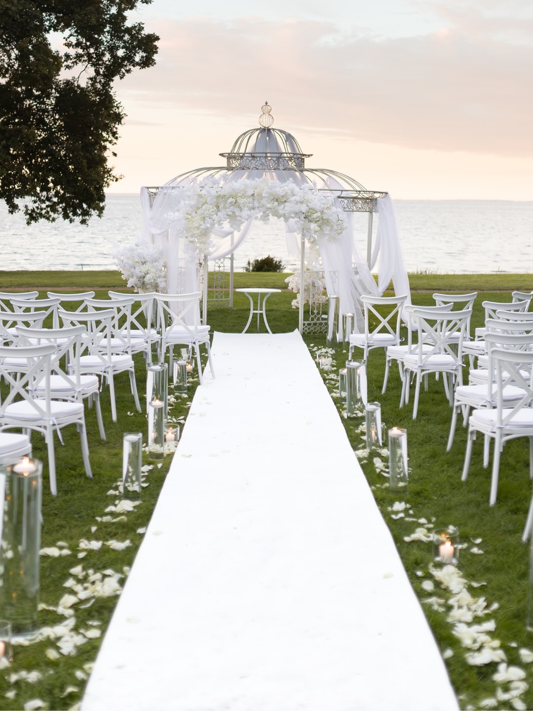 A pyramid stack of empty crystal champagne coupe glasses on a glass table with a dark background and soft lighting.