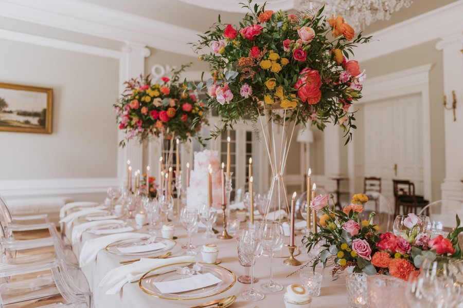 A pyramid stack of empty crystal champagne coupe glasses on a glass table with a dark background and soft lighting.