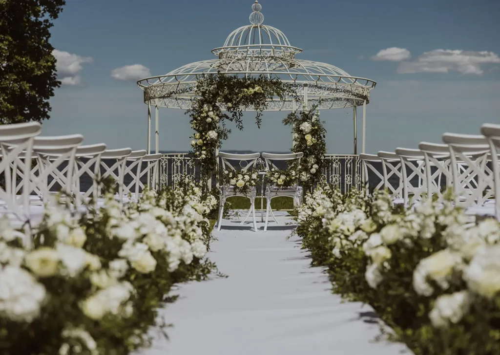 A pyramid stack of empty crystal champagne coupe glasses on a glass table with a dark background and soft lighting.