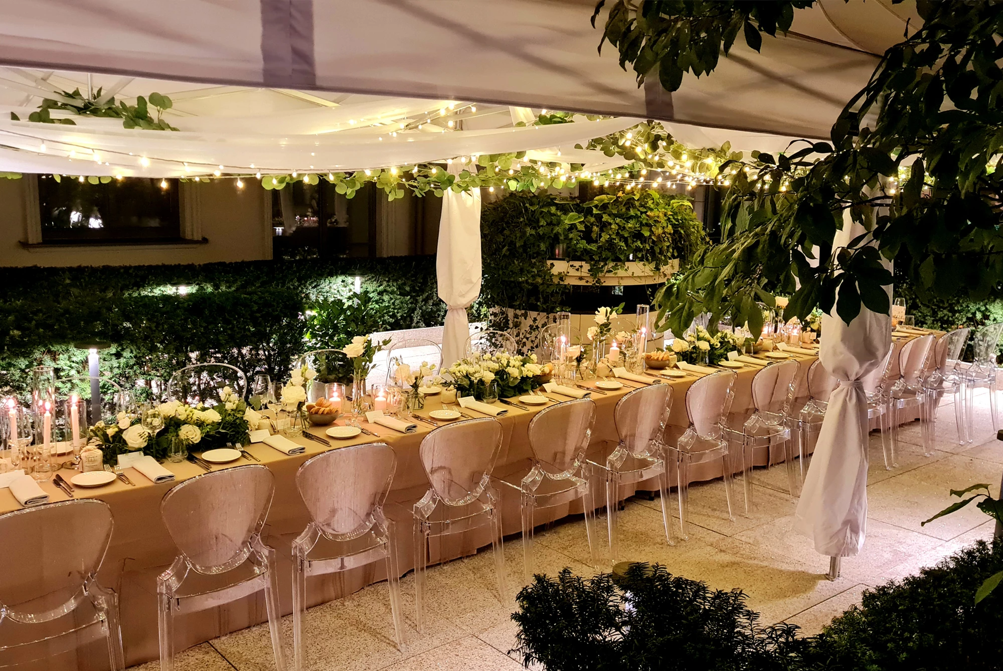 A pyramid stack of empty crystal champagne coupe glasses on a glass table with a dark background and soft lighting.