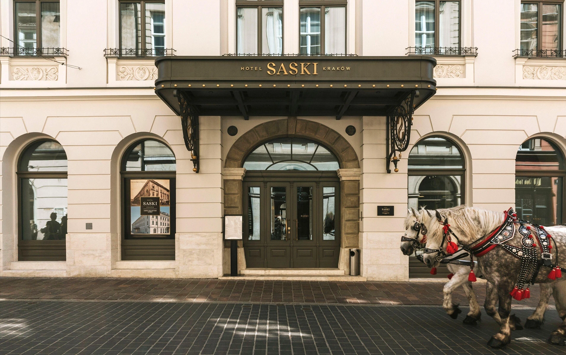 Aerial view of a historic city block with green metal roofs and a tall church tower in the background under a cloudy sky.