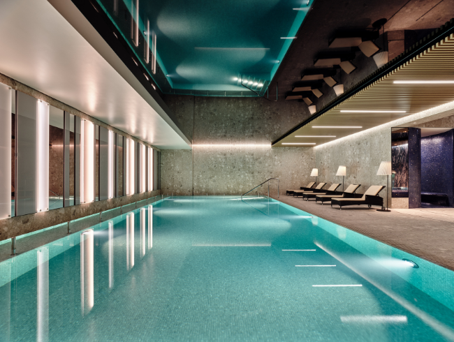 A pyramid stack of empty crystal champagne coupe glasses on a glass table with a dark background and soft lighting.