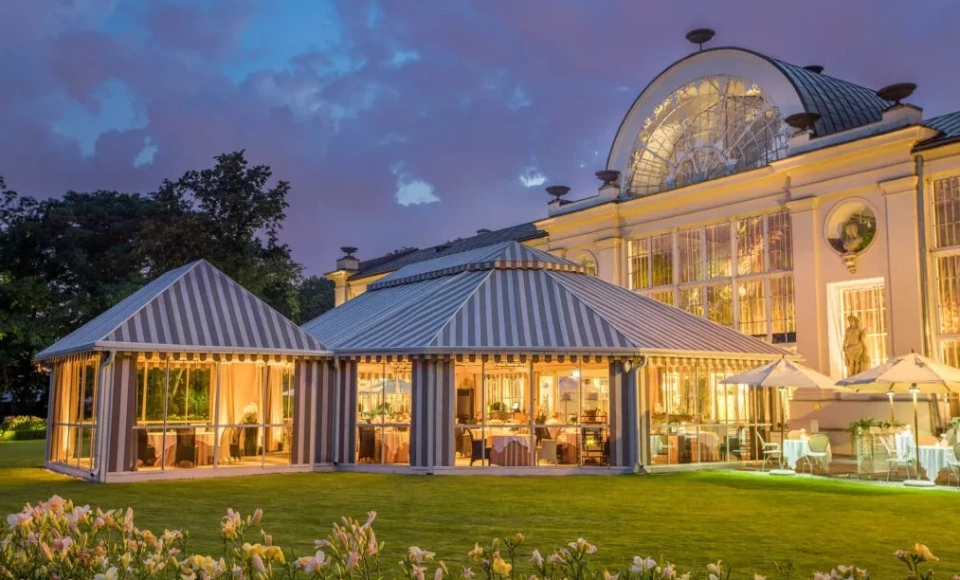 A pyramid stack of empty crystal champagne coupe glasses on a glass table with a dark background and soft lighting.