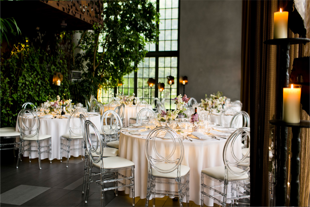 A pyramid stack of empty crystal champagne coupe glasses on a glass table with a dark background and soft lighting.