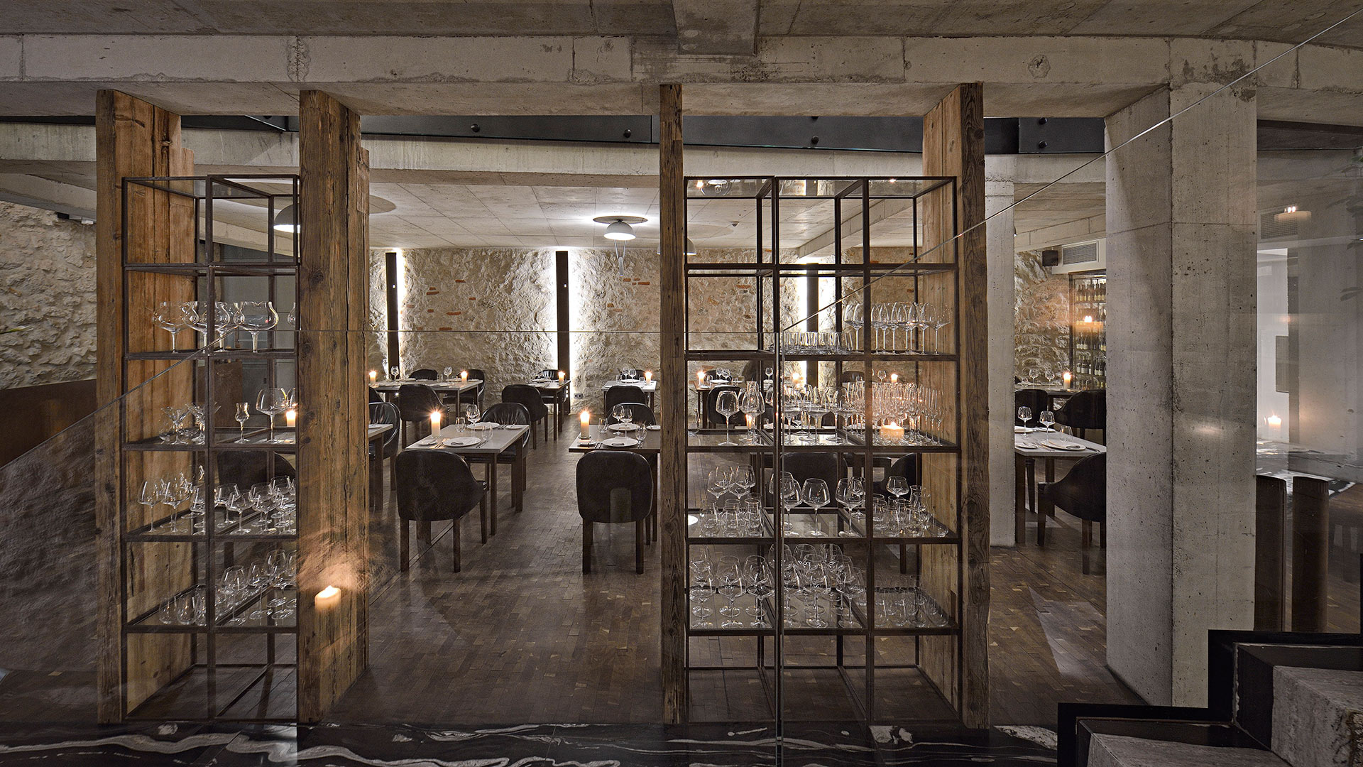 A pyramid stack of empty crystal champagne coupe glasses on a glass table with a dark background and soft lighting.