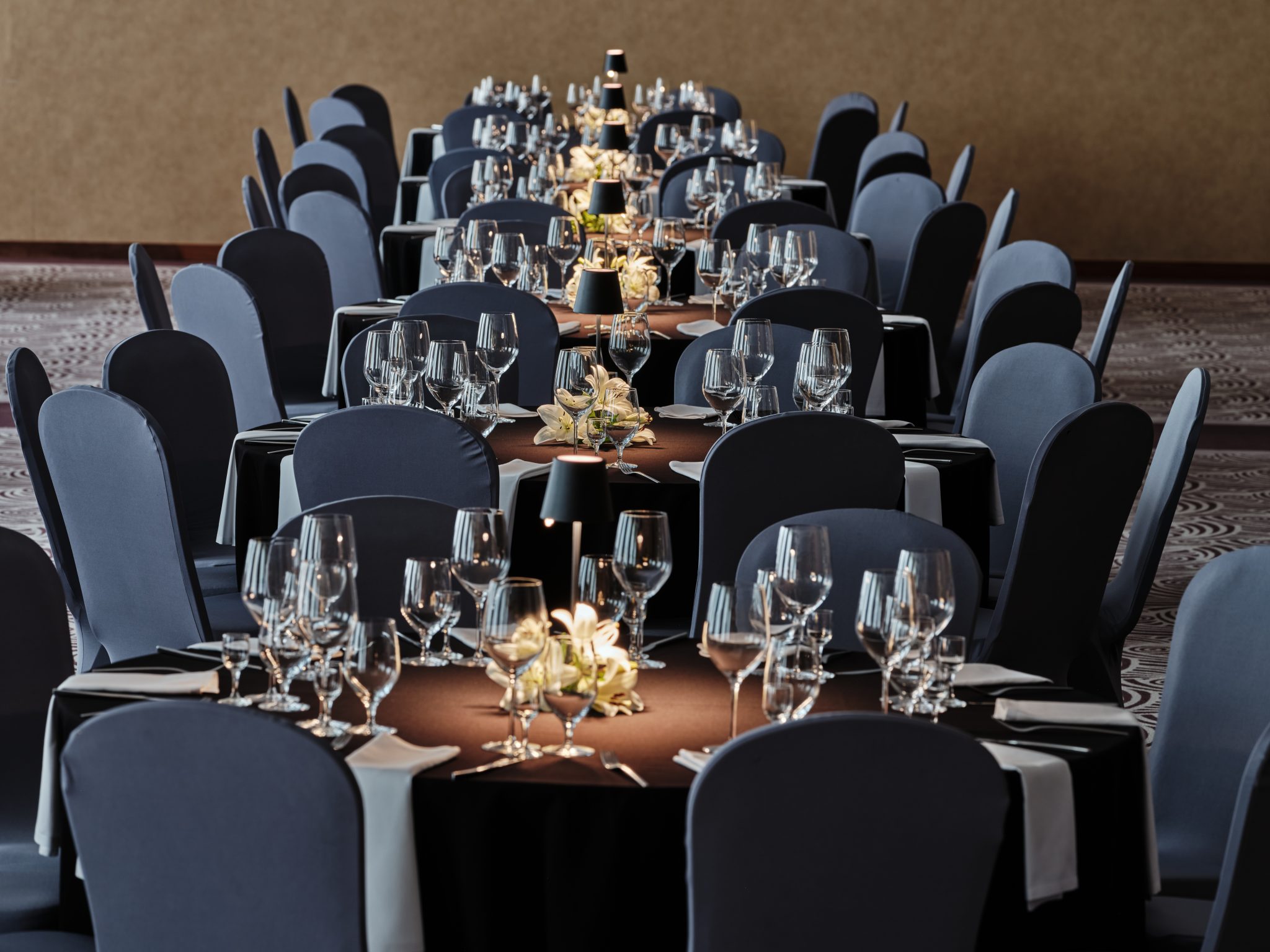 A pyramid stack of empty crystal champagne coupe glasses on a glass table with a dark background and soft lighting.