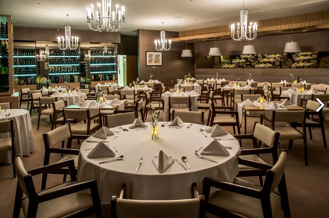 A pyramid stack of empty crystal champagne coupe glasses on a glass table with a dark background and soft lighting.