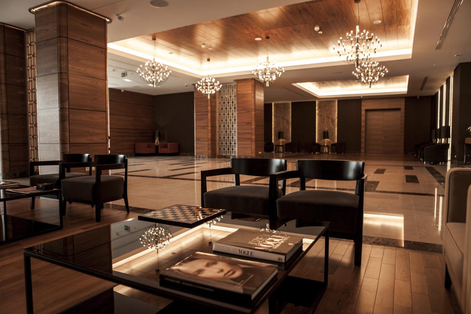 A pyramid stack of empty crystal champagne coupe glasses on a glass table with a dark background and soft lighting.