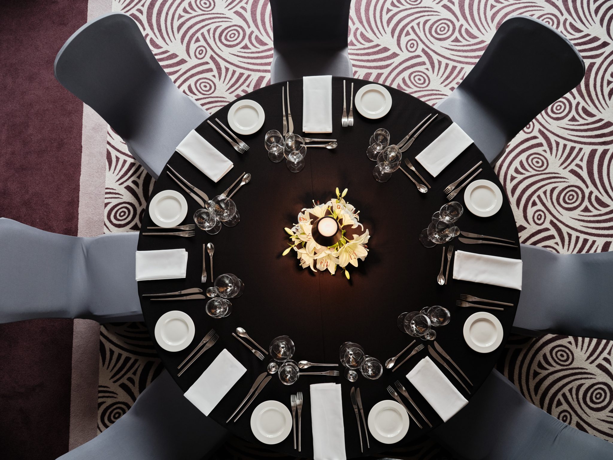 A pyramid stack of empty crystal champagne coupe glasses on a glass table with a dark background and soft lighting.