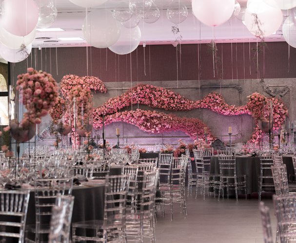 A pyramid stack of empty crystal champagne coupe glasses on a glass table with a dark background and soft lighting.