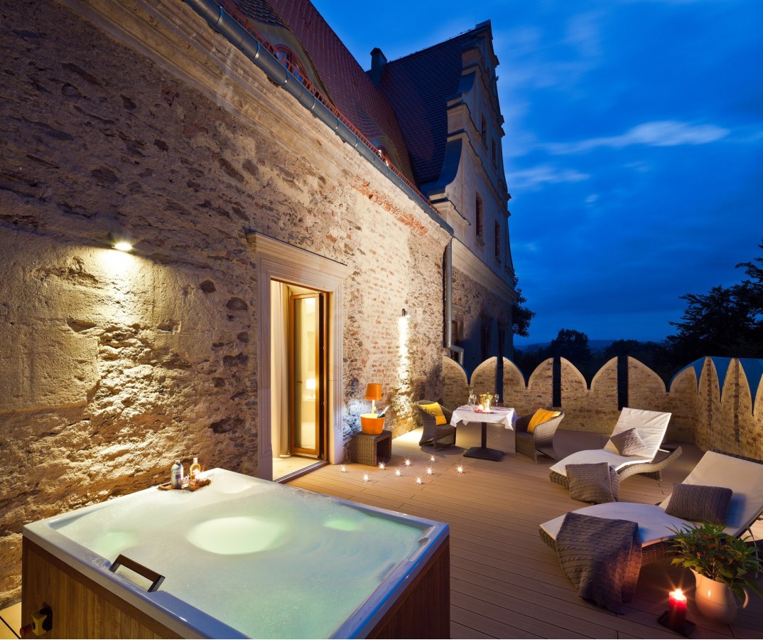 A pyramid stack of empty crystal champagne coupe glasses on a glass table with a dark background and soft lighting.