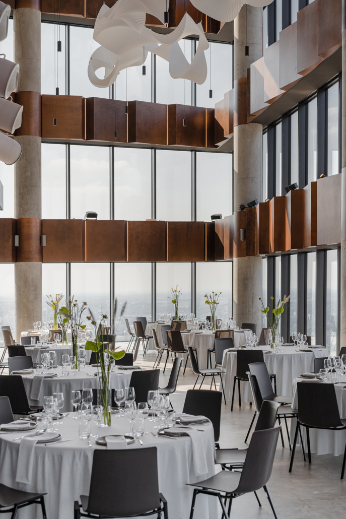 A pyramid stack of empty crystal champagne coupe glasses on a glass table with a dark background and soft lighting.