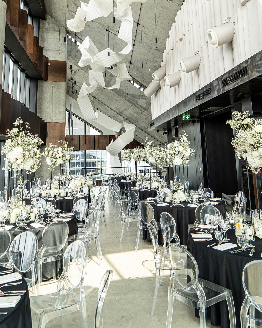 A pyramid stack of empty crystal champagne coupe glasses on a glass table with a dark background and soft lighting.