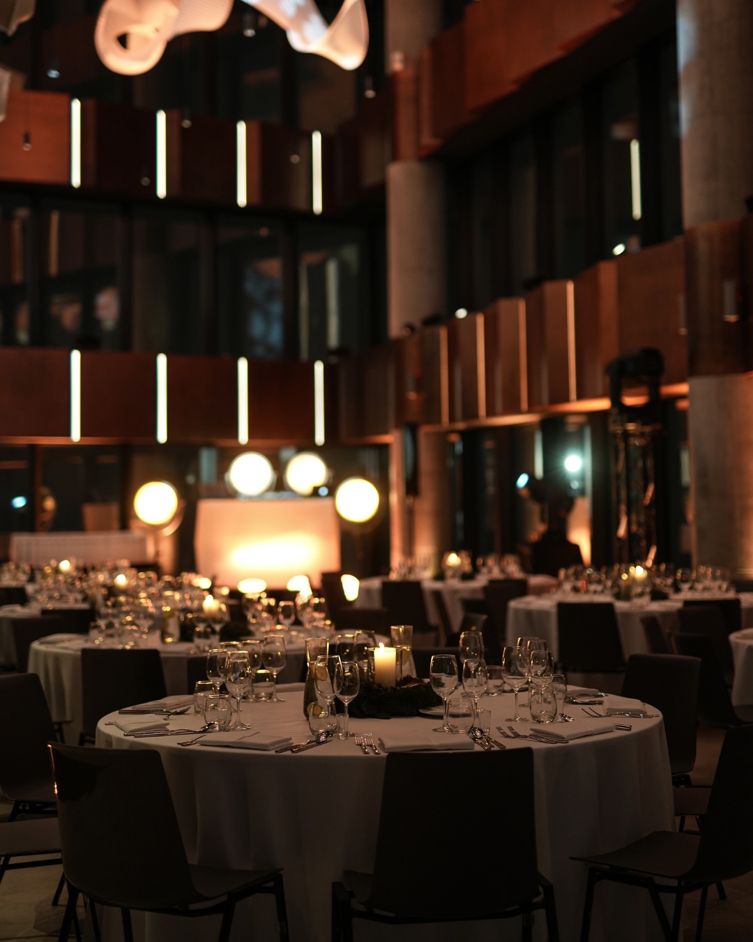 A pyramid stack of empty crystal champagne coupe glasses on a glass table with a dark background and soft lighting.