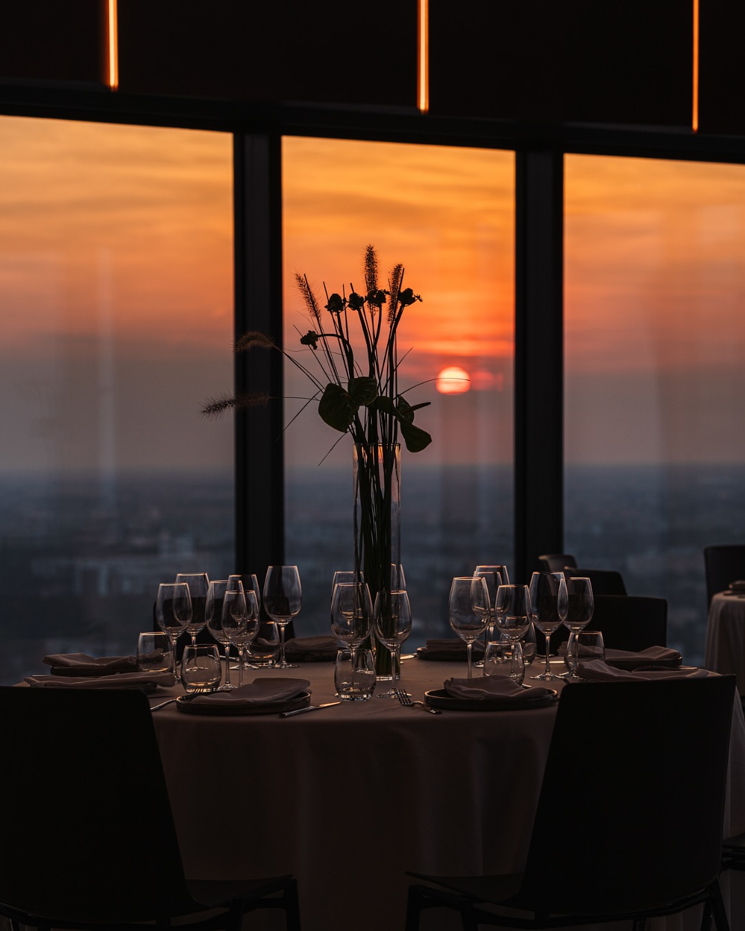 A pyramid stack of empty crystal champagne coupe glasses on a glass table with a dark background and soft lighting.